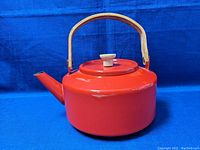 Photo of a red enamel tea kettle with wood handle, showing kettle from a side angle with spout and handle visible.