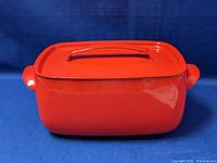 Side view of rectangular red enamel Dutch oven with lid attached, showing glossy finish and side handle.