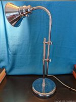 Full view of the desk lamp showing adjustable arm, gooseneck, and conical lamp shade against blue background.