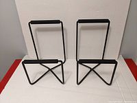 Pair of black metal speaker stands with an X-shaped base and padded top horizontal bar