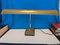 Front view of the vintage airplane-style desk lamp with military green wing-shaped fluorescent shade on a square green base with chrome adjustable arm