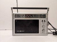 Front view of the vintage General Electric AM/FM radio showing the tuning scale, speaker grill, knobs, and power cord.