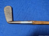 Close-up image of the metal clubhead of the vintage golf putter showing the grid pattern on the striking face and the transition from wooden shaft to metal hosel.