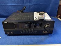 Front view of Yamaha RX-V565 AV receiver showing display, control buttons, volume knob, headphone jack, and Silent Cinema feature.