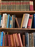 Three shelves of hardcover books, top shelf shows 23-volume uniform set with red and green cloth spines, middle and lower shelves show assorted other books