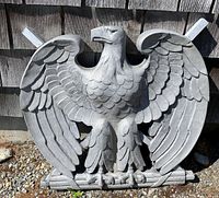 Front view of cast metal eagle sculpture against wooden wall, showing full wingspan and body detail.