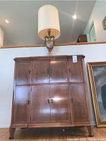Front view of wood bar cabinet with closed paneled doors and lamp on top