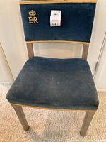 Front view of chair showing blue velvet upholstery, gold trim and embroidered insignia