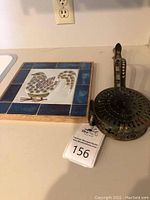 Overview of brass chestnut roaster with handle and porcelain trivet on countertop