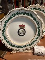 Two plates overlapping on display, showing scalloped edges and central crest