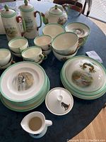 Full set arranged on table showing all items: coffee pots, teapot, mugs, saucers, bowls, plates with lapwing bird scenes and green rims