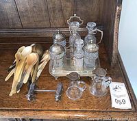 Overview of entire lot: condiment stand, cruets, dog-form bar, and shell spoons on wooden surface