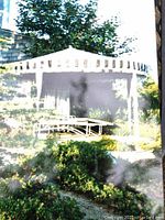 Picture of a white gazebo with striped fabric cover set up in a garden with some patio chairs inside visible through mesh sides.