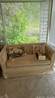 Front view of cream corduroy velvet tufted love seat with three pillows and box of pillowcases placed on seat
