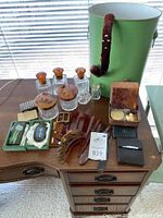 Overview of dresser top with green hatbox, glass jars, hair accessories, belt, cases and small items