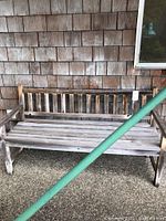 Wooden outdoor bench showing slatted back and seat, weathered wood finish, photographed against a shingle wall.