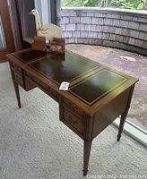 Front-left angle of desk showing leather top, drawers, goose figurine and mail sorters