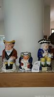 Front view of all three Staffordshire Toby Jugs on display, showing various designs and sizes