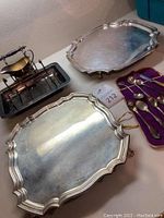 Overview of two scalloped trays, carving set in rack with gravy boat, and spoons on purple cloth