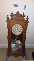 Full view of the Ansonia Queen Elizabeth wooden mantel clock showing the case, pendulum behind glass, and decorative top details.