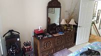 Wide shot of the dresser with attached mirror showing carved drawer fronts and various items on top.
