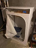 Full view of canvas clothes rack with zippered front partially open showing wooden hangers inside and plastic storage bins at bottom.