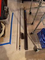 Fishing rod disassembled into two pieces with case on right side, displayed on carpet.