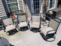 Four black metal frame patio swivel chairs with grey mesh seats lined up on deck