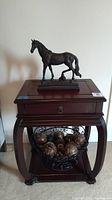Bronze horse sculpture displayed atop the wooden nightstand with decorative spheres holder on lower shelf
