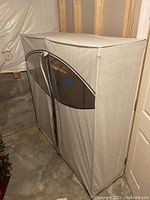 Front view of covered clothes rack showing beige cover with clear plastic window and clothes inside on hangers.