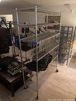 Overall angled view of the chrome metal wire rack showing all four shelves, caster wheels, and part of the surrounding room environment.