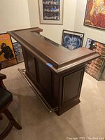 L-shaped wooden home bar with dark brown finish and foot rail shown from angled front side.