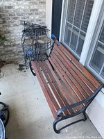 Outdoor bench with wooden slats and black metal frame positioned on patio beside a window, showing the overall structure and condition of the bench.