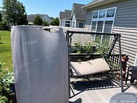 Full view of the outdoor rocking bench with beige cushions and the attached shade canopy fabric leaning nearby.