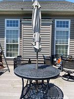 Full view of round metal outdoor table with closed beige umbrella attached through center.