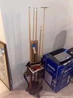 Full view of six pool cues standing in the pool cue holder with some accessories and other items on top