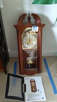 Full front view of the wooden swan neck chiming clock with brass pendulum and open front door showing glass insert.