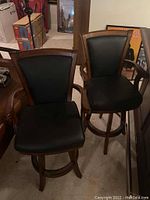 Two matching wooden bar stools with black upholstered padded seats and backs, shown side by side.
