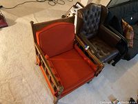 Photo showing both chairs side by side: the brown leather tufted armchair and the wooden framed orange cushioned chair.