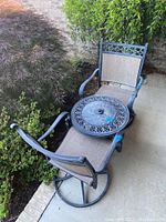 Photo showing two swivel outdoor chairs with mesh seating and ornate metal detailing, along with matching round metal table with decorative tabletop.