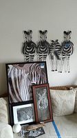 Wall-mounted metal zebras and multiple framed zebra artworks leaning on a couch