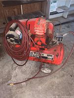 Photo showing front left side of Montgomery Ward red air compressor with hose coiled on the unit.