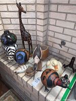 Photo showing the full assortment of animal figurines and the decorative vase arranged on a tiled surface against a brick wall.