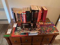 Books arranged on a wooden chest showing a mix of novels, reference books, and catalogs with visible wear.