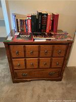 Front view of wood chest of drawers showing three drawers with metal handles, items on top for scale but not included.