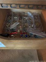Drawer with clear plastic organizer containing multiple compartments filled with assorted costume jewelry pieces including earrings, bracelets, and pins.
