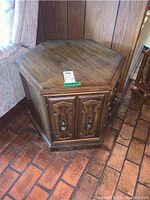 Photo of one hexagonal wooden end table showing wood grain top, carved cabinet doors with metal handles, sitting on a reddish tiled floor.