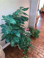 Two faux greenery plants of different sizes shown against a wall, large plant on left and smaller plant on right.
