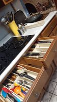 Open kitchen drawers displaying assorted wooden and plastic cooking utensils such as spatulas, spoons, measuring spoons, and cutters.