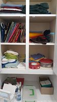 Shelves with folded towels, colorful gift bags, scarves, small paint bottles, tins, and storage containers.